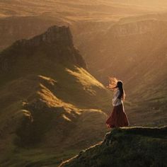 a woman standing on top of a mountain with her hair blowing in the wind,