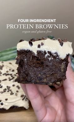 a hand holding a piece of brownie with white frosting