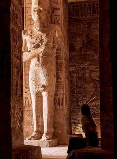 a woman sitting in front of an ancient statue