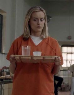 a woman in an orange prison uniform holding a tray with two cups on it and another person standing behind her