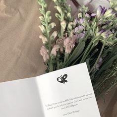 an open book sitting on top of a table next to some purple and white flowers