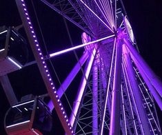 a ferris wheel lit up at night with purple lights on the top and bottom part