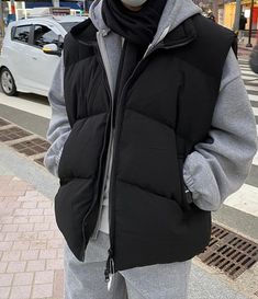 a man standing on the street wearing a black jacket and grey pants with a white mask