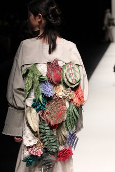 a woman is walking down the runway in a dress made out of flowers and leaves