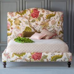 a bed with floral upholstered headboard and foot board, sitting in front of a gray paneled wall