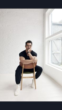 a man sitting on top of a wooden chair in front of a white brick wall