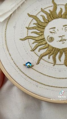 someone is stitching a sun face on a white piece of fabric with gold thread