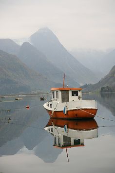 an orange and white boat sitting on top of a body of water next to mountains