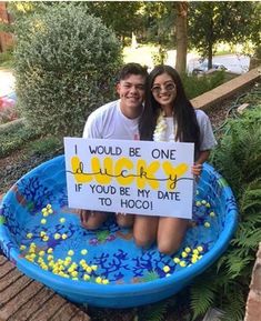 two people sitting in a pool holding a sign that says i would be one lucky if you'd be my date to hoo