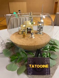 a table topped with a glass bowl filled with toys and plants next to a sign that says tatooine