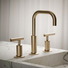 two brass faucets on a marble counter top