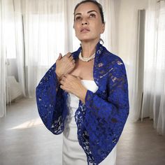 a woman wearing a blue jacket standing in front of a window with her hands on her chest