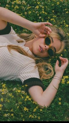 a woman laying in the grass with her hands on her head and looking into the camera