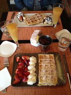 some waffles and strawberries are sitting on a table with glasses of orange juice