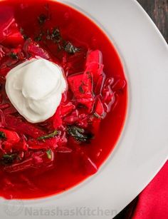 a white plate topped with red soup and sour cream on top of it's side