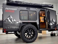 an off road camper trailer is parked in a garage with its doors open and mountains painted on the side