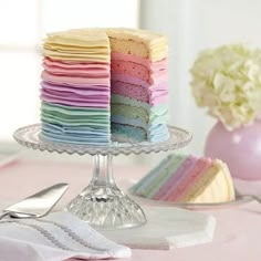 a multi - colored cake is on a glass plate with silverware and flowers in the background