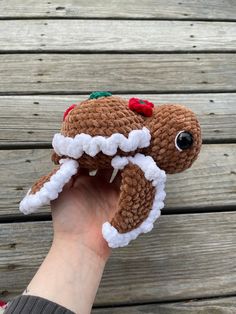 a hand holding up a brown and white crochet christmas ornament on wood planks