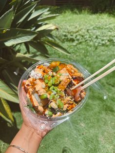 a person holding up a bowl of food with chopsticks