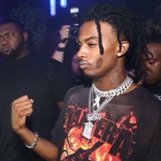 a young man with dreadlocks standing in front of other people at a party