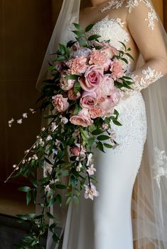 a woman in a wedding dress holding a bridal bouquet with pink roses and greenery