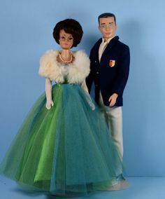 two dolls are posed next to each other on a blue background and one is wearing a green dress