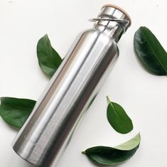 a stainless steel flask with leaves around it on a white surface, surrounded by green leaves