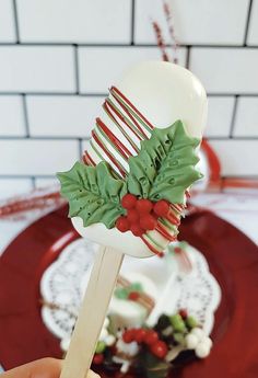 a hand holding a candy cane decorated with holly and mistlet leaves on top of a red plate