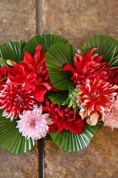 red and pink flowers are arranged in a fan shaped arrangement on a tile floor with green leaves