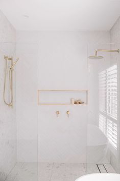 a white tiled bathroom with gold fixtures and shower faucet in the corner, along with shelving on the wall