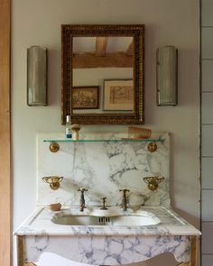 a bathroom with marble counter top and gold faucet, mirror above the sink