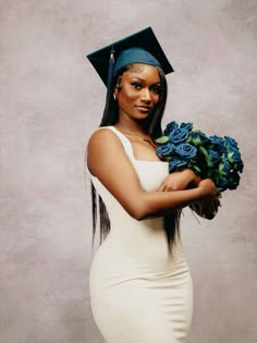 a woman wearing a graduation cap and gown holding blue roses in her right hand while posing for the camera