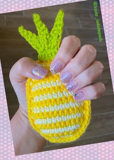 a hand holding a yellow and white crocheted pineapple with green leaves on it