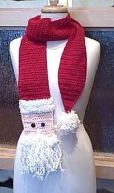 a red scarf with white trim and a santa clause on the front is sitting on a mannequin