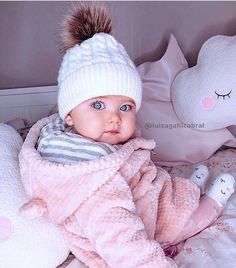 a baby in a pink coat and hat laying on a bed next to stuffed animals