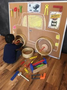 a young boy is playing with toys in front of a bulletin board on the floor