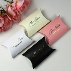 three different colored business cards sitting next to pink flowers on top of a white table