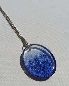 a necklace with blue glitter on it sitting on a white surface