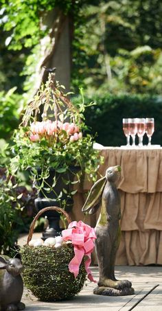 a statue of a rabbit holding a pink bow in front of a table with wine glasses on it