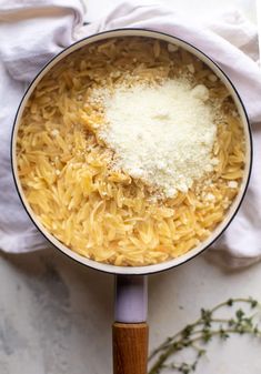 a pot filled with pasta and cheese on top of a white table cloth next to a wooden spoon