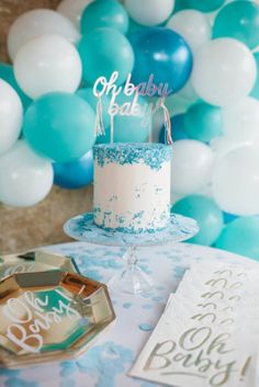 a blue and white cake sitting on top of a table with balloons in the background