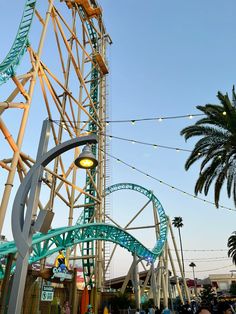 the roller coaster at an amusement park with palm trees in the foreground and people walking around