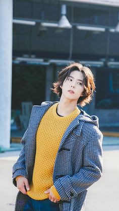 a young man standing in front of a building wearing a yellow sweater and blue jeans