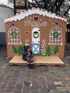 a person sitting in front of a house made out of cardboard and decorated with candy canes