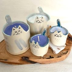 a wooden tray topped with white and blue ceramic cat cups on top of each other