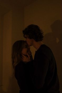 two people are kissing in the dark with their shadows on the wall and one person is holding his hand up to his face