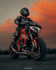 a man riding on the back of a red and black motorcycle under a cloudy sky