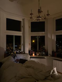 an unmade bed sitting in front of three windows with lights shining on the outside