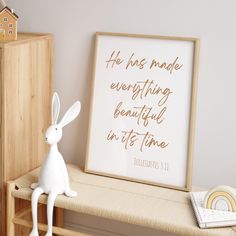 a white rabbit figurine sitting on top of a wooden bench next to a framed poster