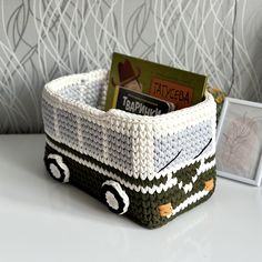 a knitted basket sitting on top of a white table next to a photo frame